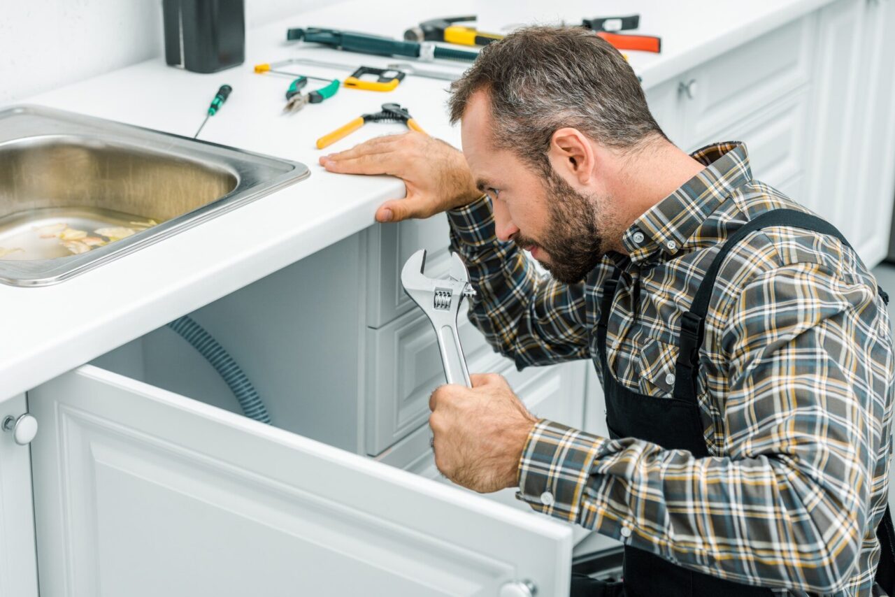 Inspector assessing plumbing and moisture beneath a kitchen sink